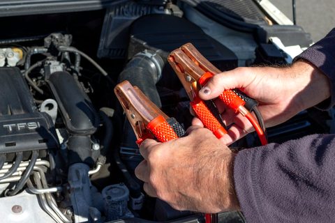 Hands holding red and black jumper clamps over an engine